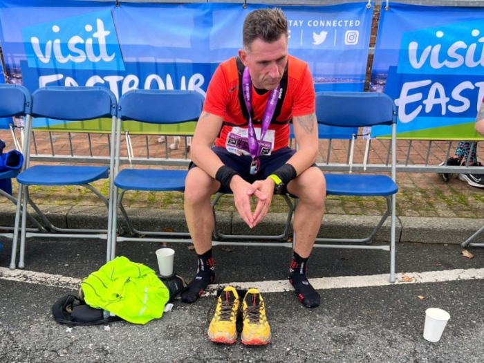 Ex-footballer Nicky Forster sitting on a bench after a run. His yellow running shoes are laid out in front of him. 